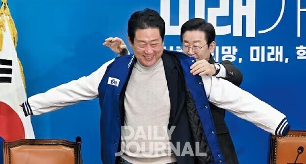 22대 총선을 두 달 앞둔 2024년 2월 14일 이재명 당시 민주당 대표가 유동철 동의대 교수에게 당 점퍼를 입혀주고 있다.